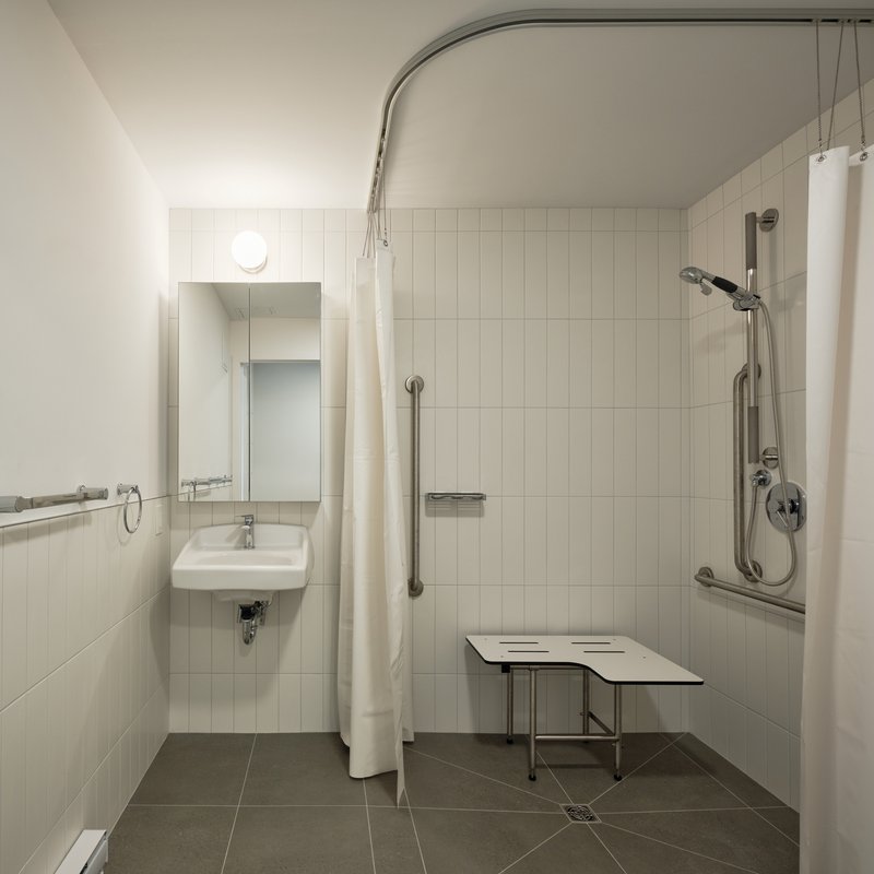 Accessible bathroom with wall-mounted sink, curved curtain rail, grab bars, and fold-down shower bench