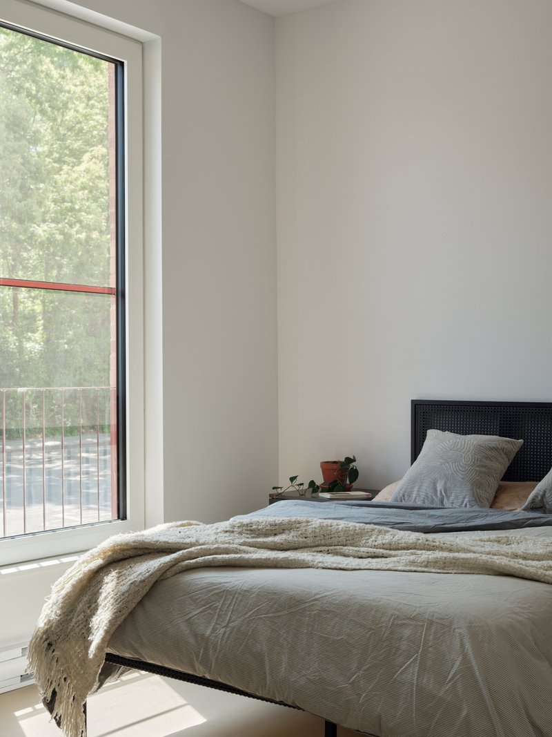 Bedroom with tall window overlooking balcony railings and trees in soft daylight