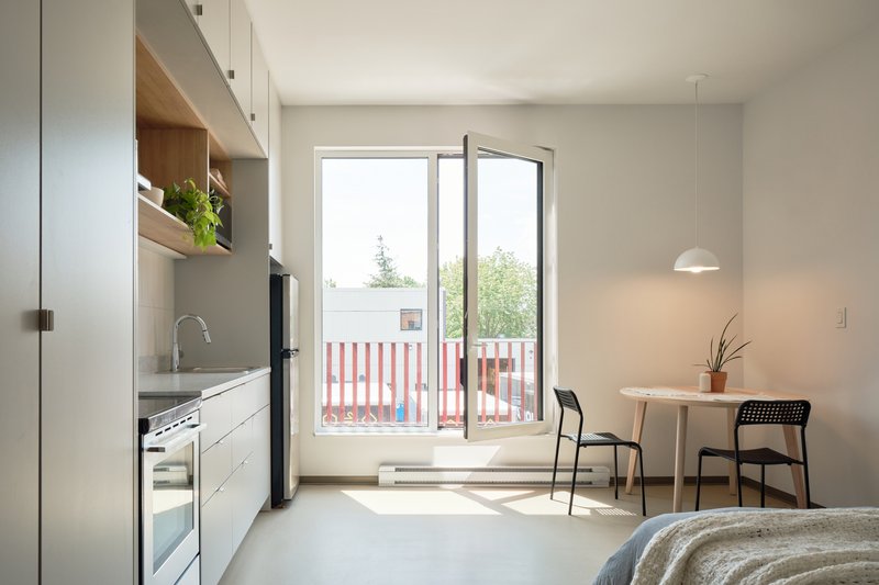 Studio unit with galley kitchen and glazed door opening to balcony with vertical railings
