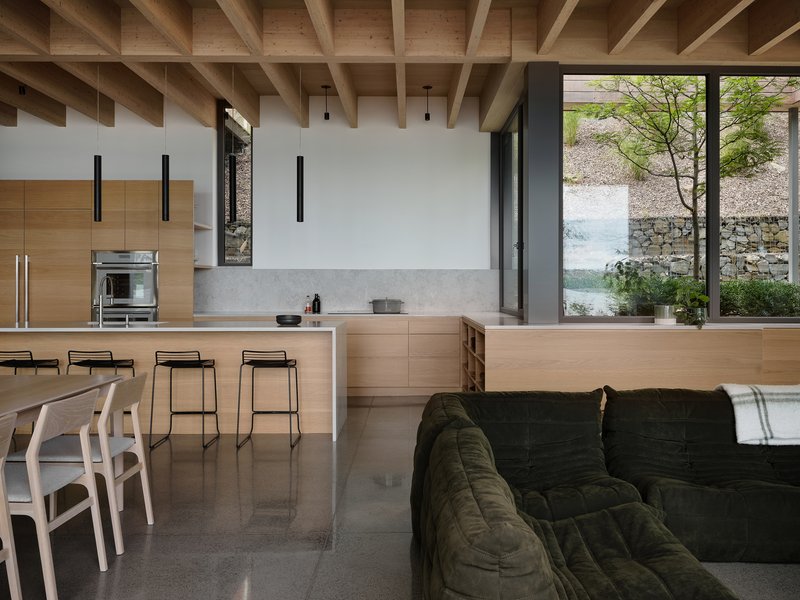 Open-plan kitchen and living space with exposed timber ceiling joists and polished concrete floor