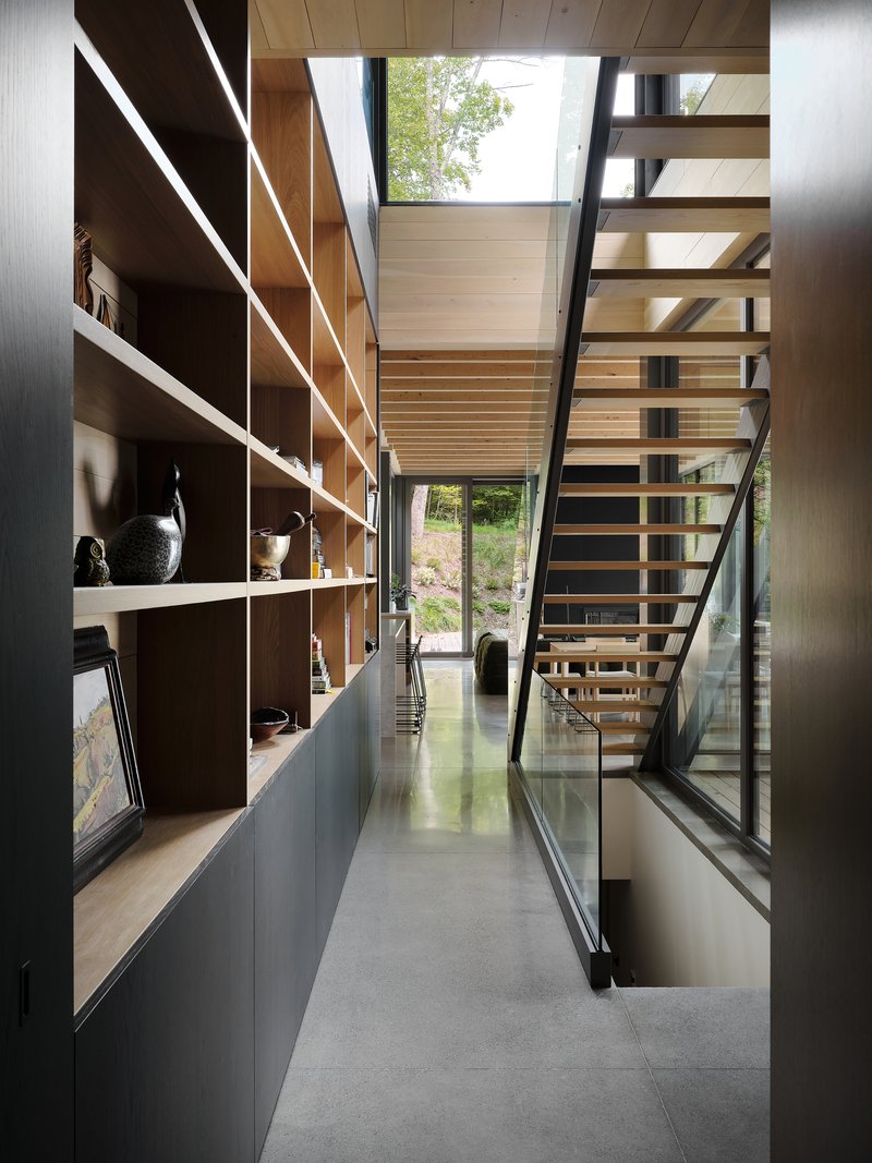Narrow corridor with open-tread timber stair alongside built-in shelving illuminated by natural light from above
