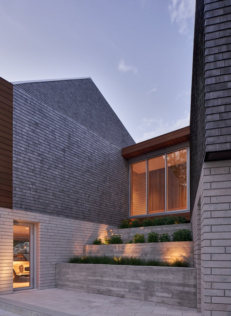 Courtyard view of textured concrete planter walls with lighting beneath planted beds at dusk