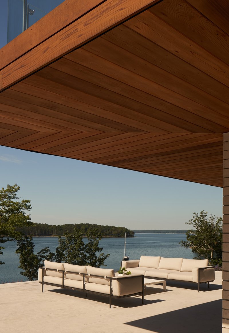 Covered terrace with timber ceiling and outdoor seating overlooking a forested lake in clear daylight