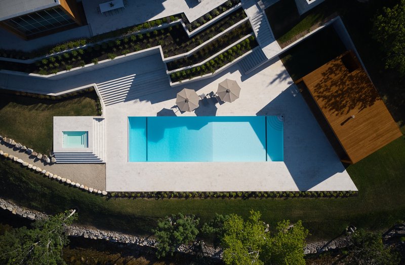 Overhead view of the pool terrace with lounge seating and planted retaining walls descending to the shoreline