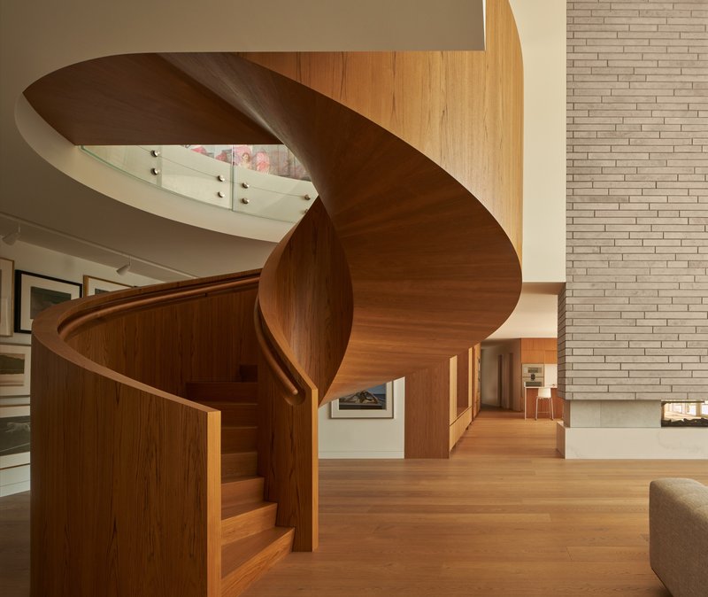 Freestanding helical timber staircase beside the brick wall in the double-height living space
