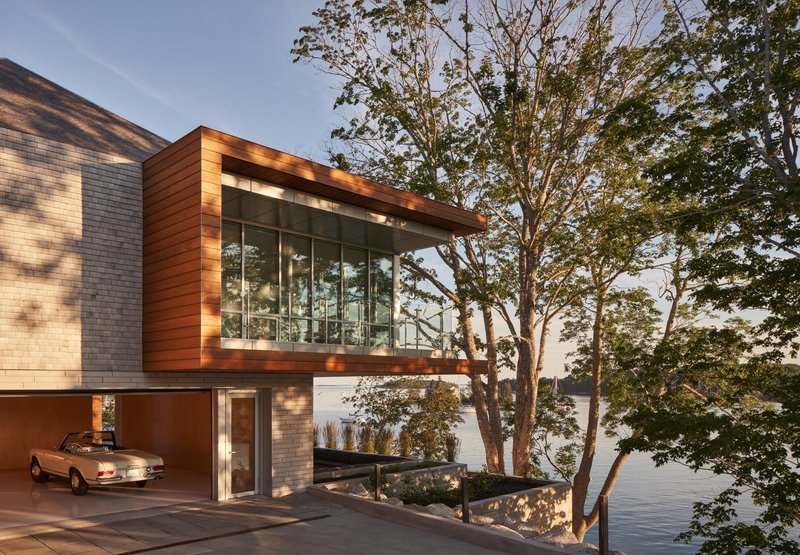 Cantilevered wood-clad volume with floor-to-ceiling glazing beside an existing birch tree at dusk