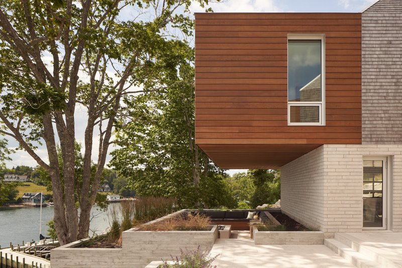 Cantilevered wood-clad box above a limestone base and waterside planting beds with lake beyond