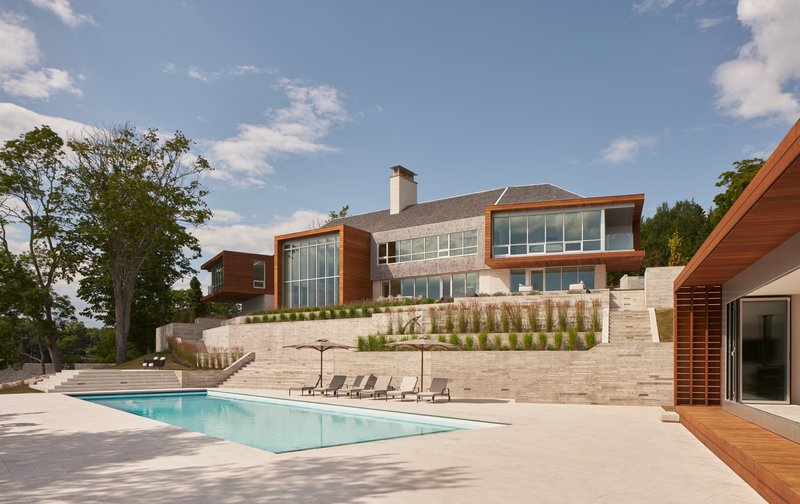 Rear view of the residence with tiered limestone retaining walls and rectangular pool under afternoon sun