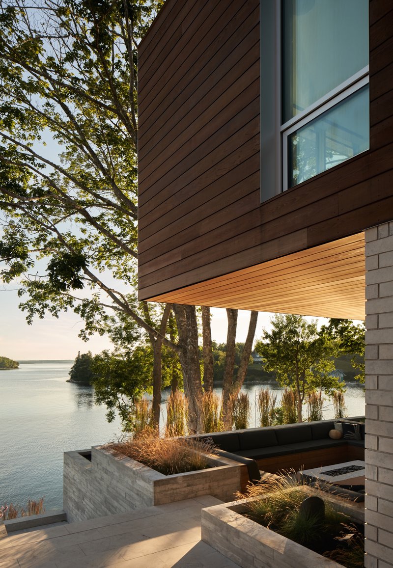 Cantilevered wood soffit above planted concrete beds with ornamental grasses facing the lake at dusk