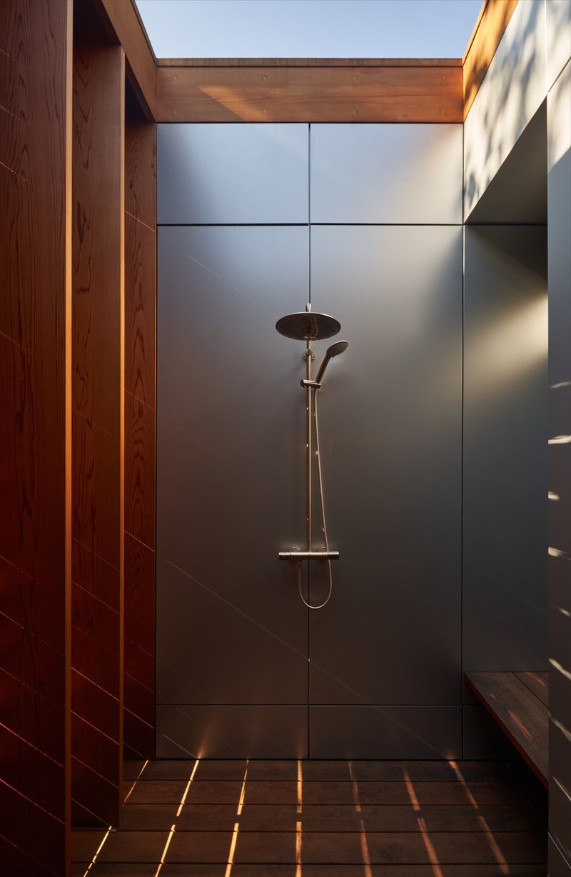 Outdoor shower stall with dark tile walls and timber ceiling open to sky