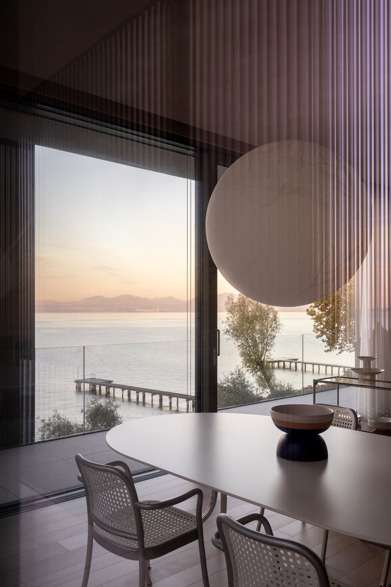 Dining area framed by sheer curtains with lake view, timber pier and distant hills at dusk
