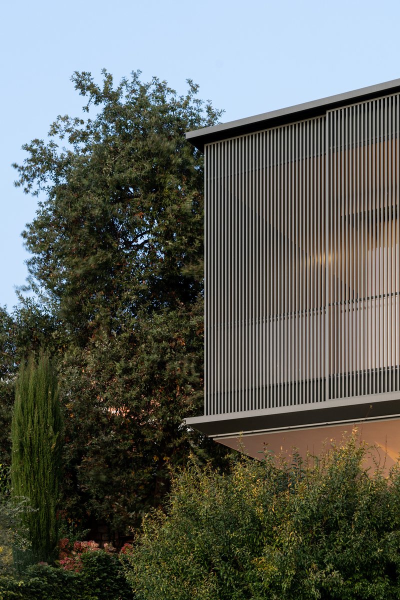 Elevated volume with vertical timber louvres above garden planting and mature trees under blue sky