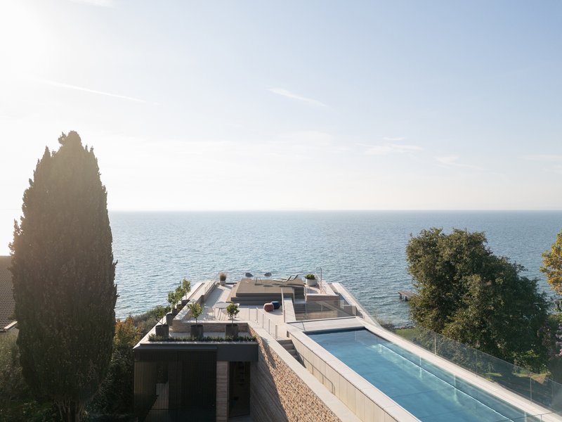 Aerial view of the rooftop terrace with pool and glass-edged parapet facing the waterfront at dusk