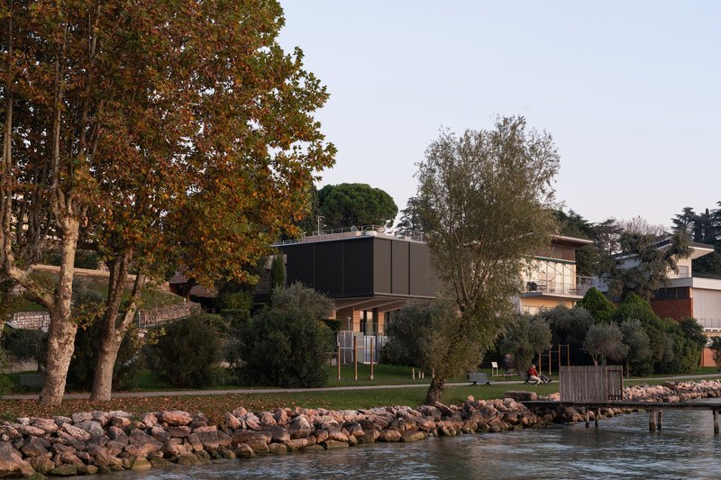 Elevated volume on pilotis viewed from the rocky waterfront with autumn trees and lawn