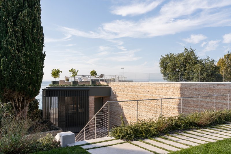Planted roof terrace above rammed earth retaining wall with stepping stone path and cypress