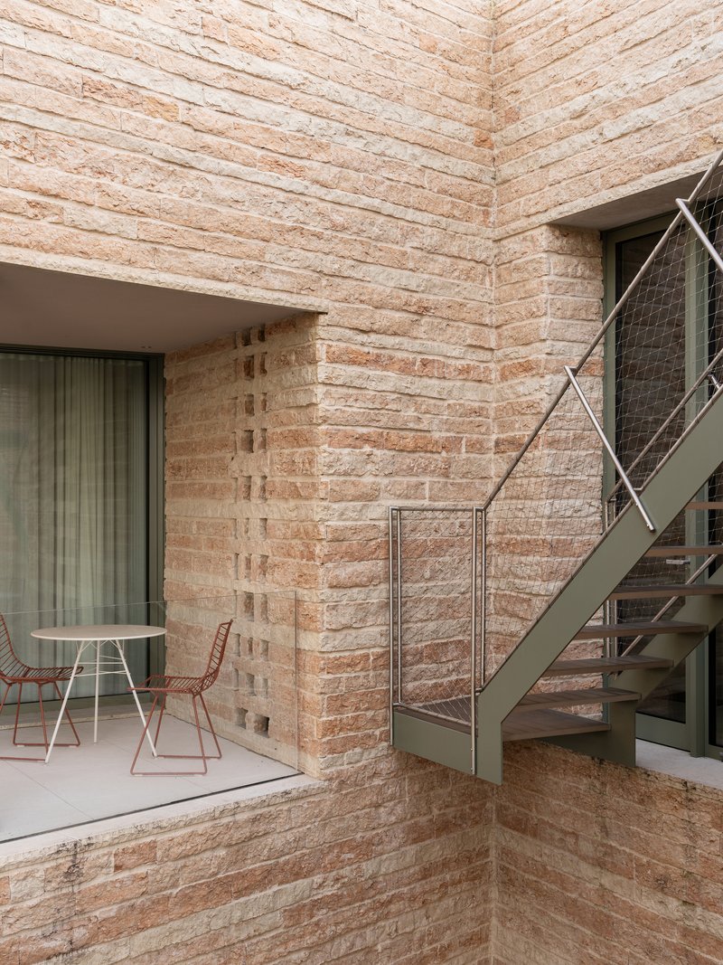Courtyard corner with layered stone walls, a metal staircase, and a table set beneath a recessed balcony