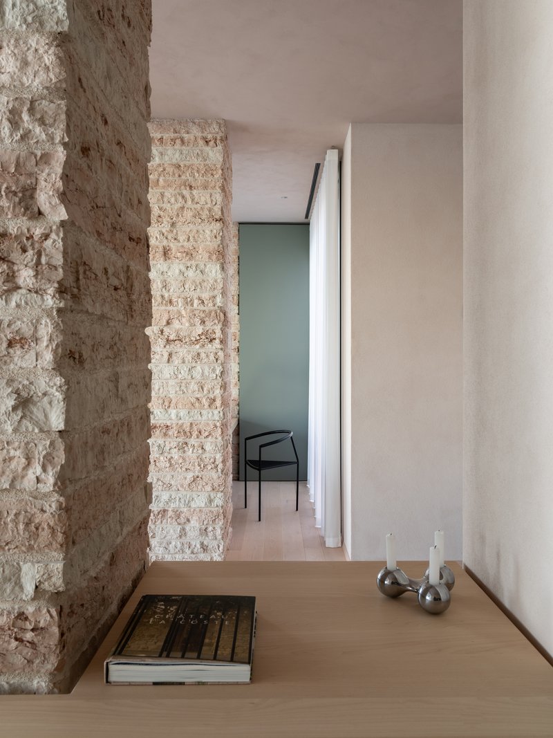 Hallway threshold between rough stone wall and smooth white plaster with a doorway visible beyond