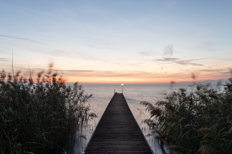 Timber boardwalk extending through reeds toward the lake at sunset