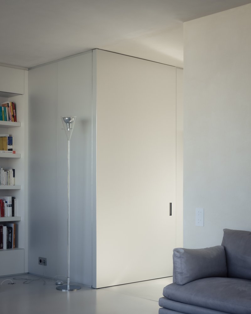 Corner of living space with white sliding panel and chrome floor lamp beside built-in bookshelf