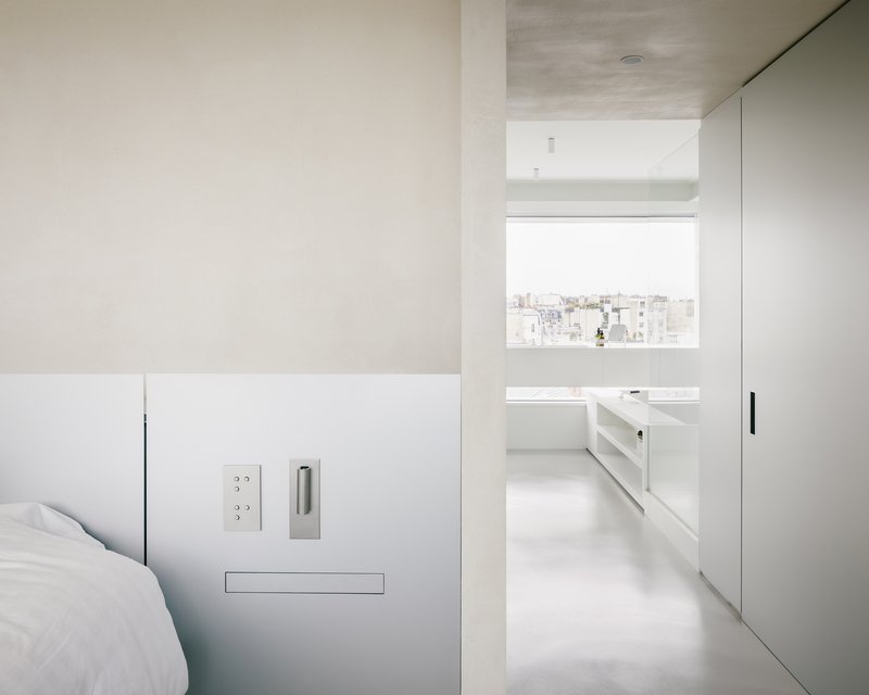 View through bedroom doorway into bathroom with window framing distant rooftops