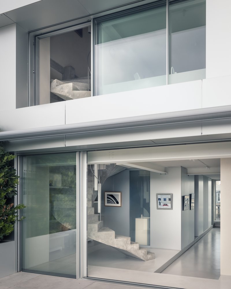Two-story facade with sliding glass doors revealing a poured concrete staircase and art-hung interior
