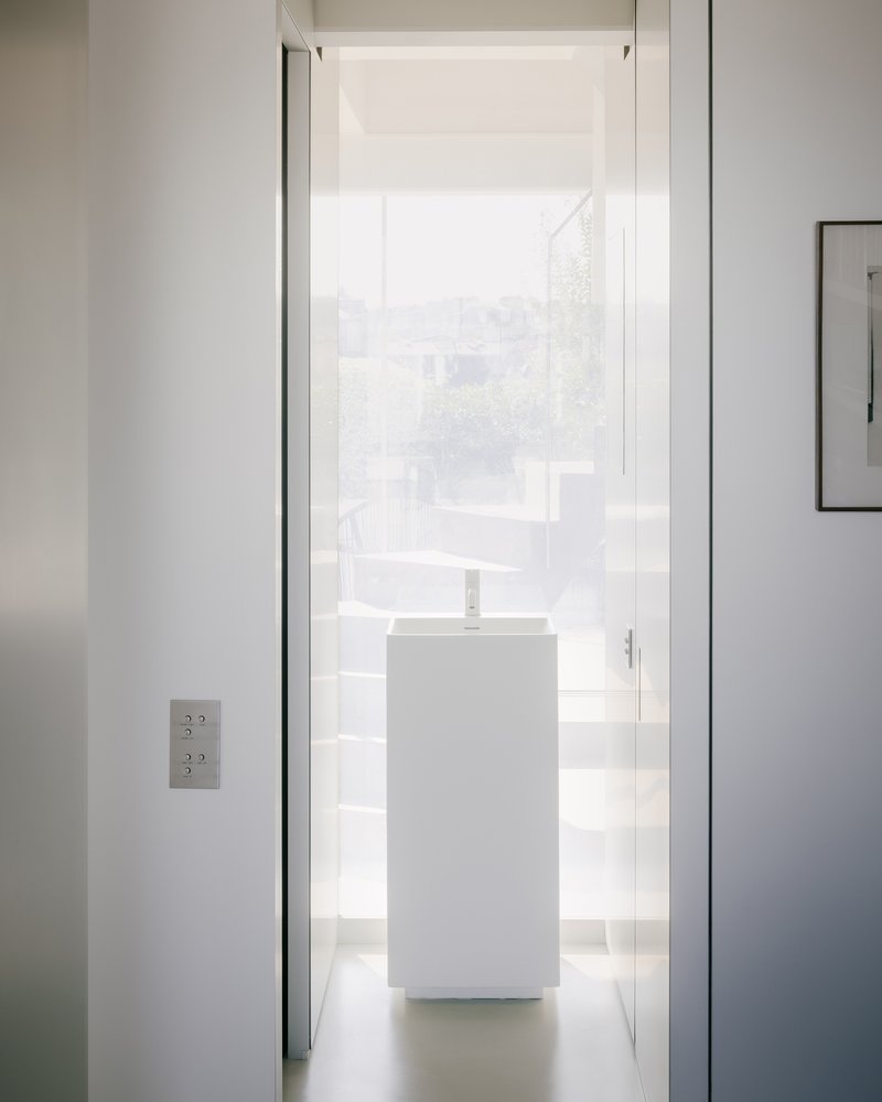 Narrow corridor with white pedestal sink framed by doorway under diffused natural light