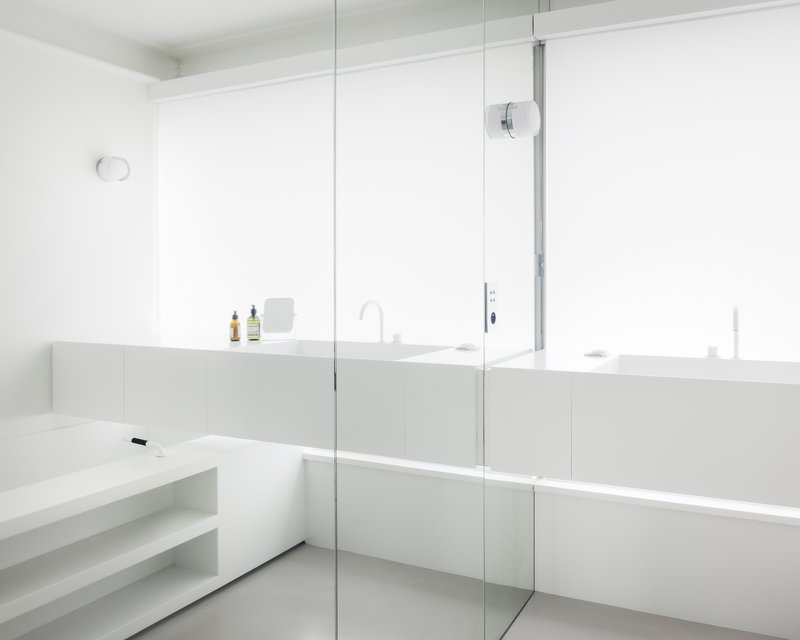 Bathroom vanity with glass shower partition and continuous horizontal mirror under recessed lighting