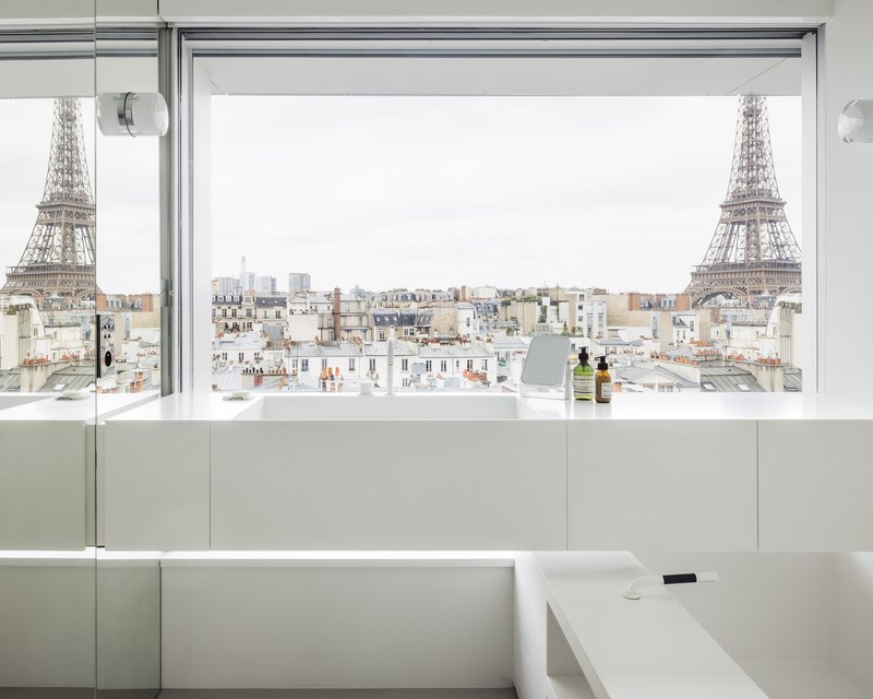 Bathtub edge and window opening framing rooftops and tower beyond under overcast sky