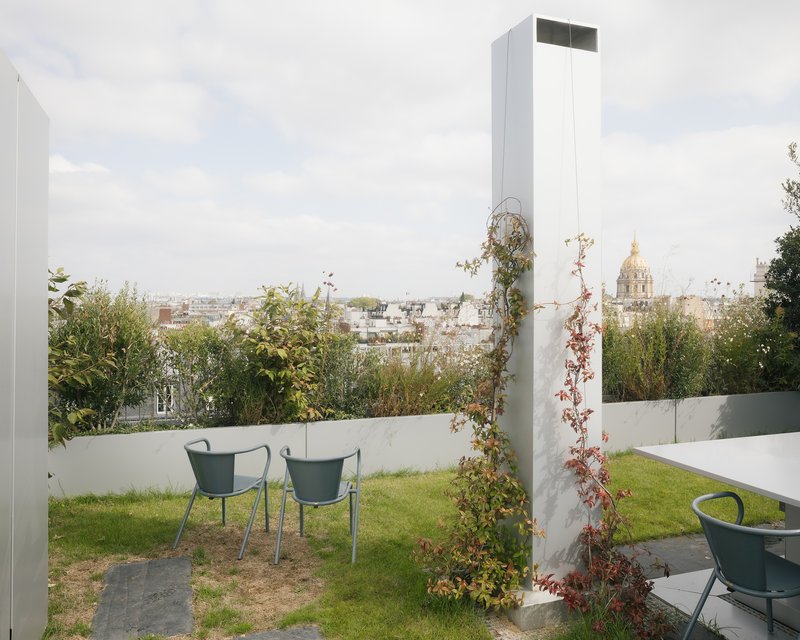 Rooftop garden with two green chairs and planted beds overlooking the urban skyline under overcast skies