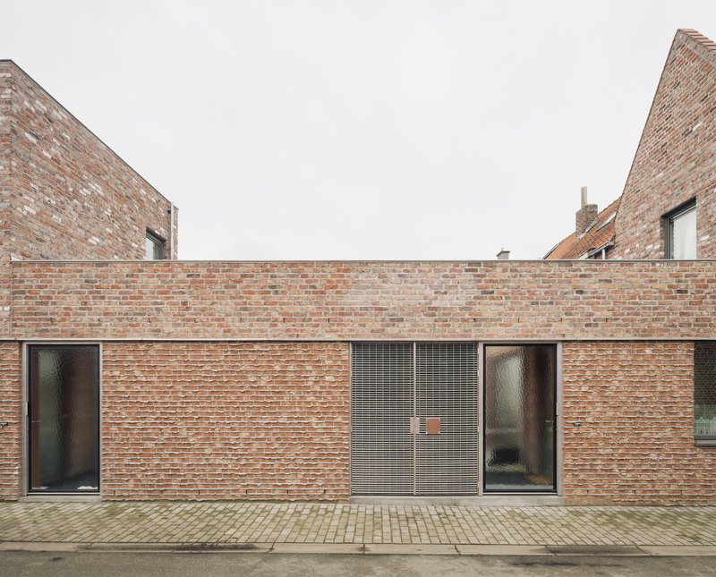 Courtyard elevation with corrugated metal shutters and two doors set within variegated brick walls under grey sky