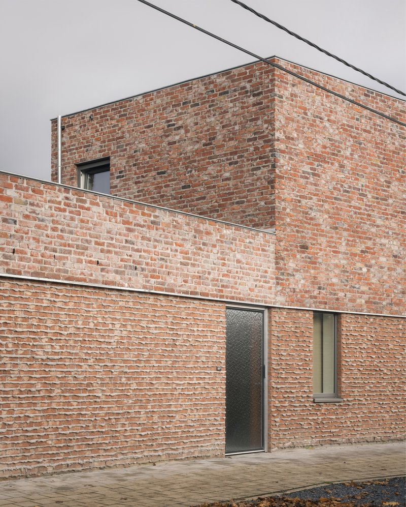 Brick facade volumes with recessed openings and overhead power lines against a pale sky