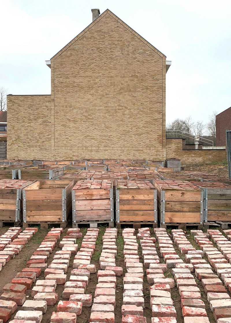 Courtyard with timber formwork planters and rows of laid bricks fronting a brick gable wall