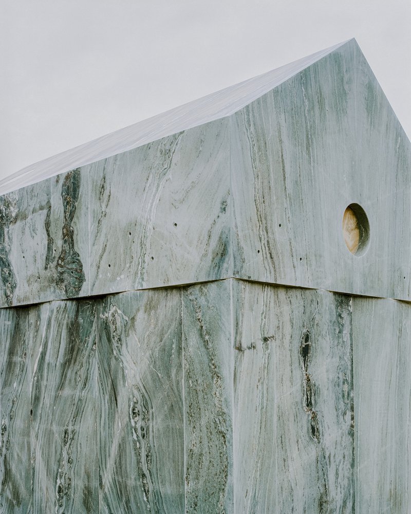 Detail of the upper corner where marble panels meet at the gable edge with circular oculus