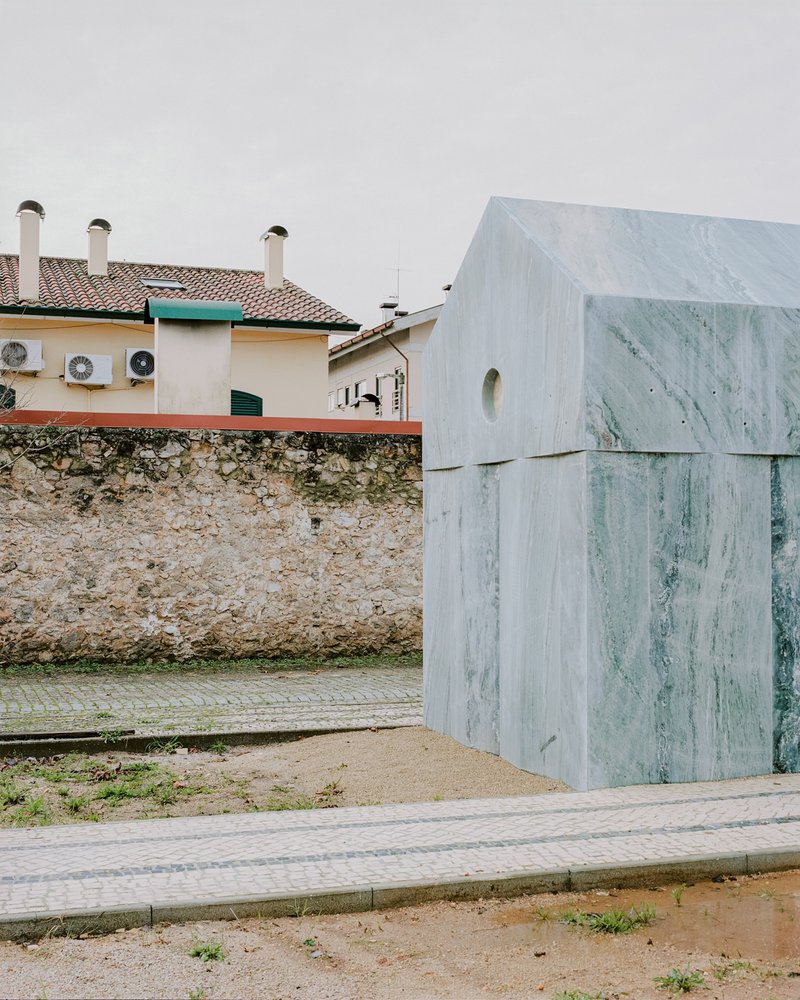 Side elevation showing layered marble panels against a weathered stone boundary wall and neighboring houses