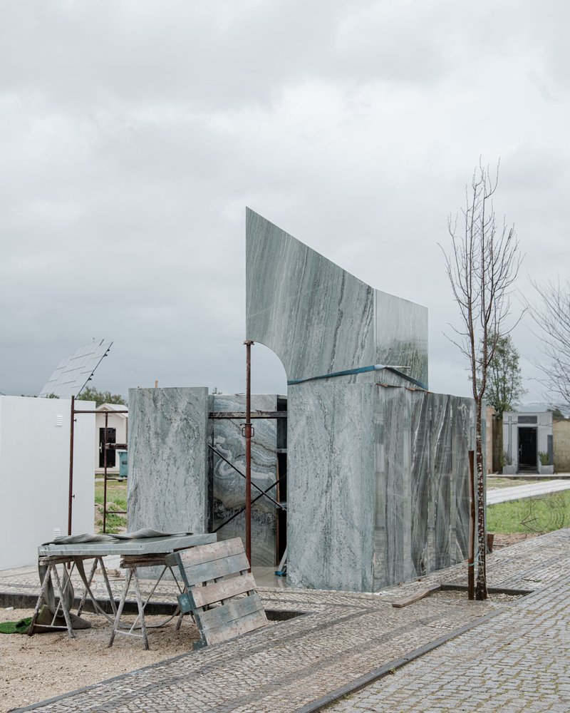 Curving volumetric facade clad in veined grey marble panels under construction on a cloudy day