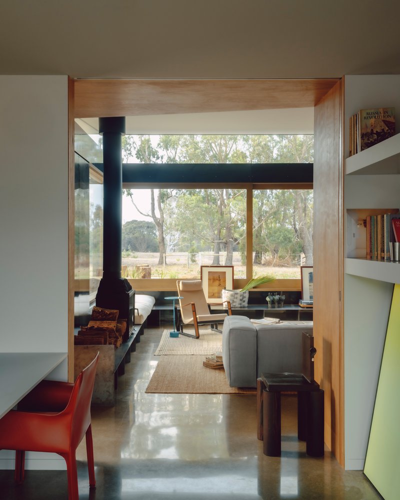 Axial view through living room with timber-lined ceiling portal and freestanding stove on polished concrete