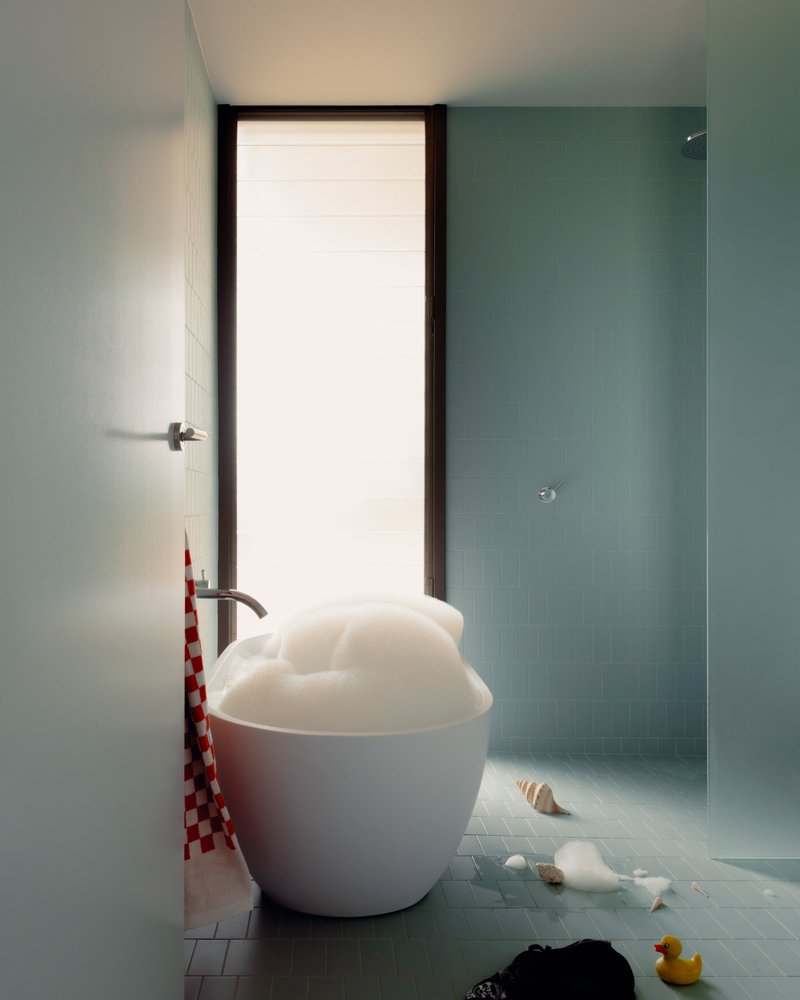 Bathroom with white spherical tub and pale blue mosaic tiles beneath a tall frosted window