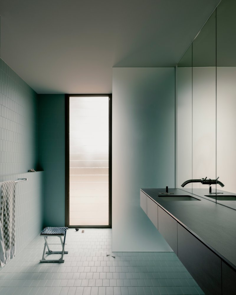 Bathroom vanity in pale blue with white subway tiles and mirrored wall beside a doorway