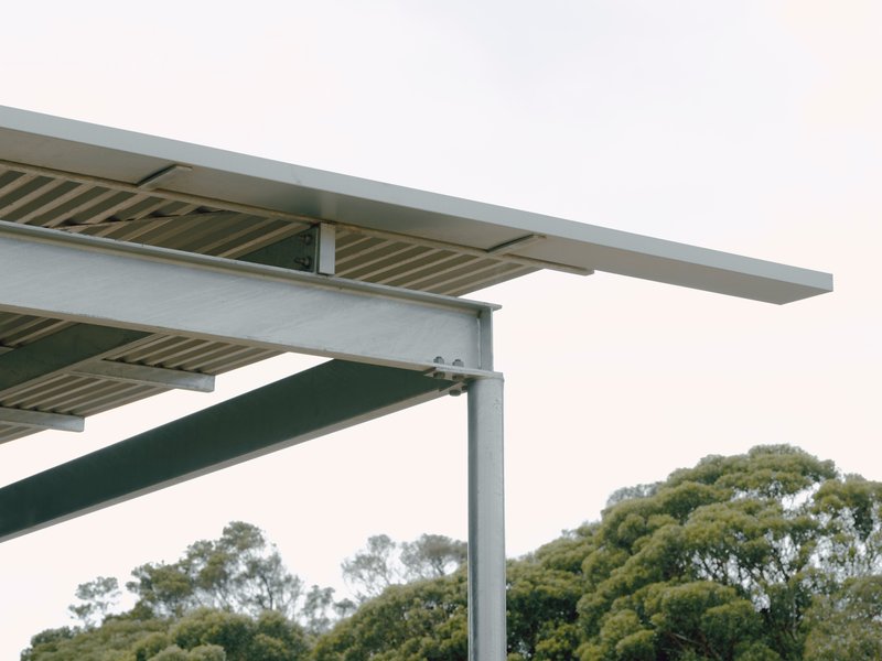Detail of steel beam and timber slat canopy against overcast sky with treetops beyond