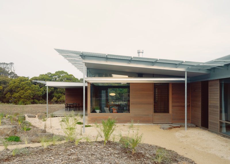 Entrance facade with horizontal timber cladding and covered steel-framed porch beside newly planted native grasses