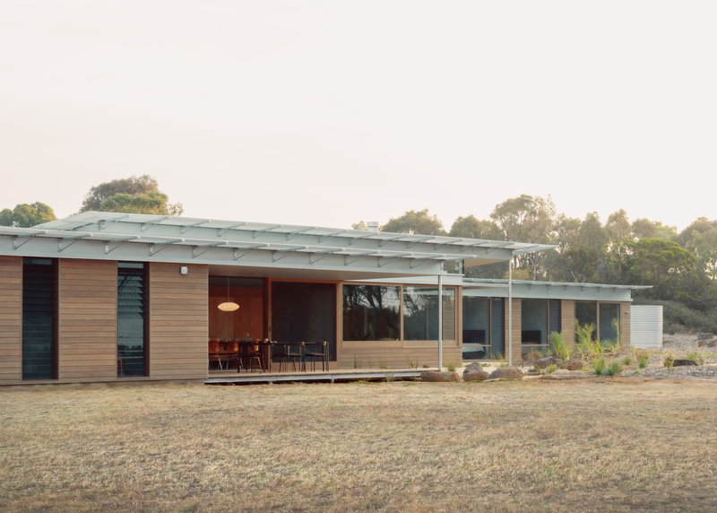Long elevation showing timber-clad volumes beneath a low-pitched metal roof at dusk