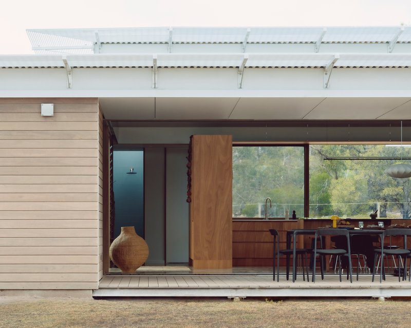 Timber deck threshold between interior kitchen and exterior wall clad in pale horizontal boards