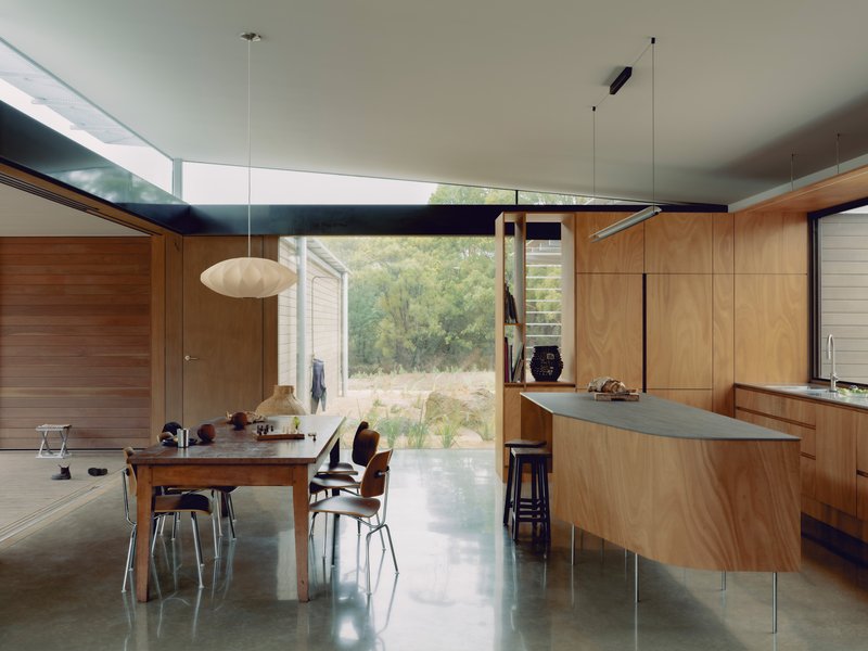 Open-plan kitchen and dining space with timber cabinetry beneath a horizontal clerestory window