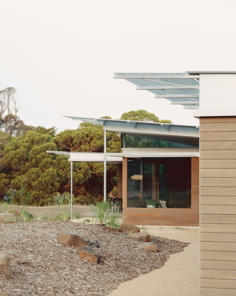 Angled rooflines with metal canopies and planted gravel beds beside horizontal timber cladding