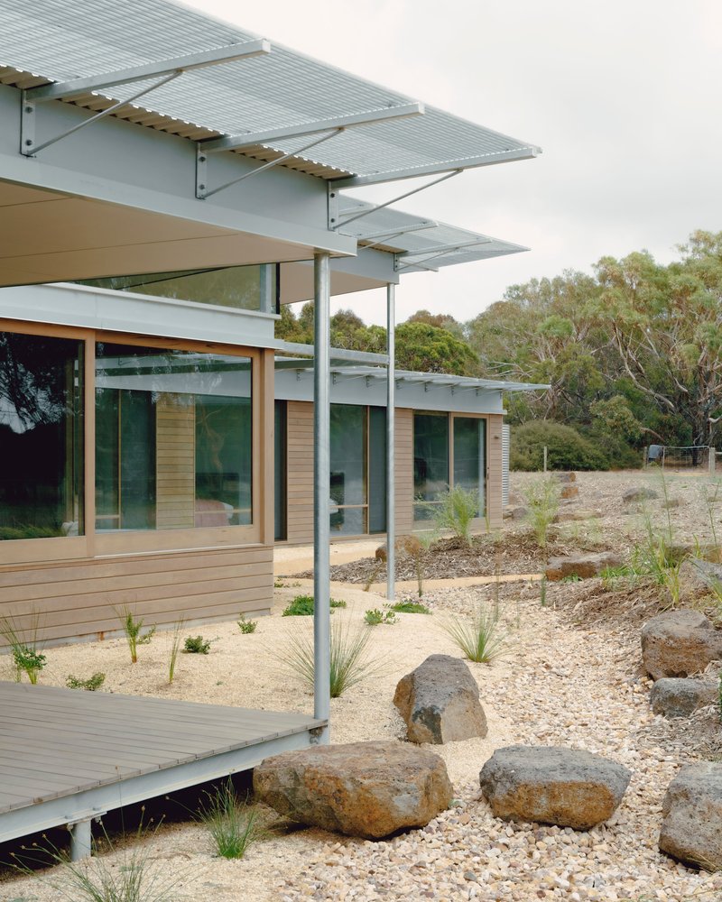 Exterior deck with perforated metal canopy supported by slender steel columns above a gravel garden