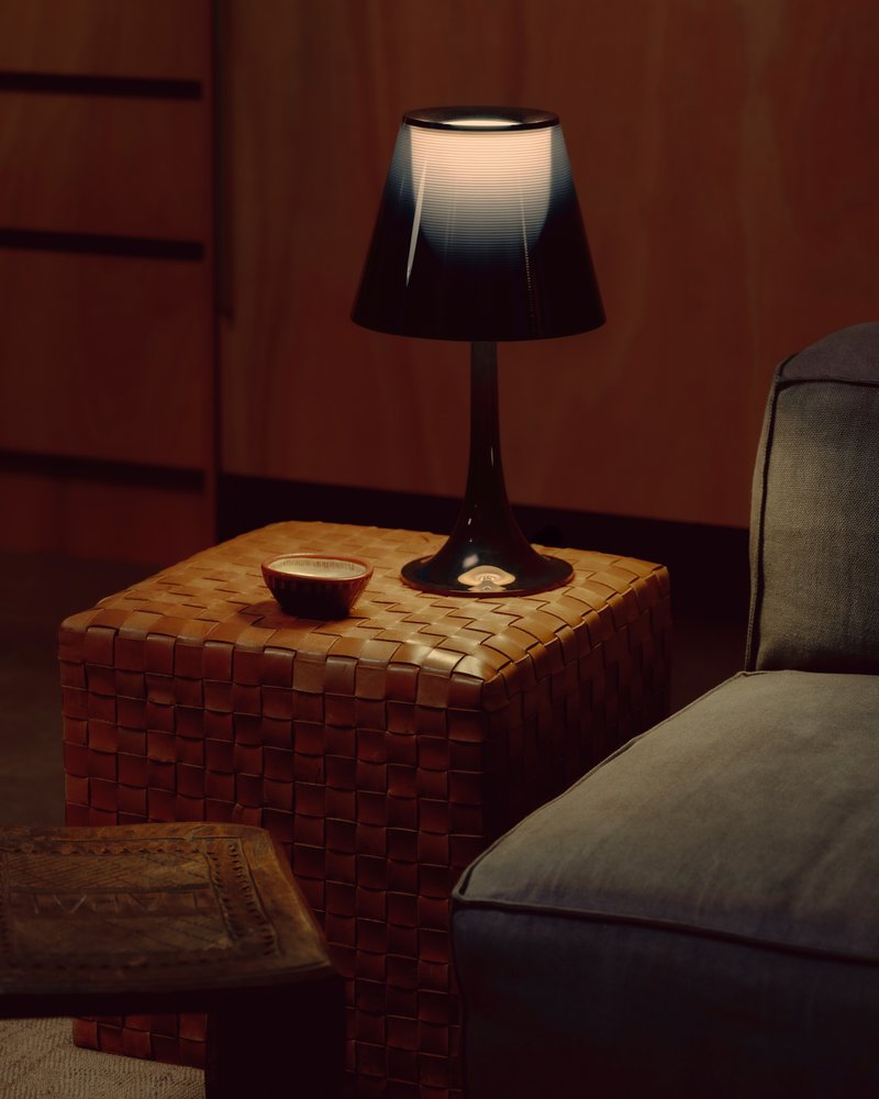 Woven leather side table with illuminated table lamp and ceramic bowl against a timber paneled wall