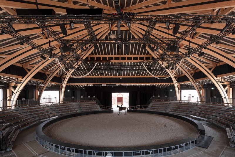 Interior of the circular arena with exposed timber rafters, steel trusses, and tiered seating under clerestory roof