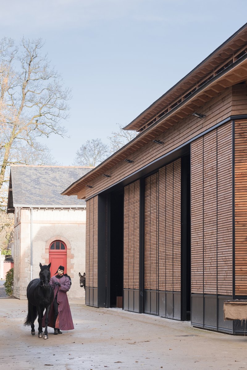 Corner of the timber structure with sloping roof and handler with horse beside the entrance