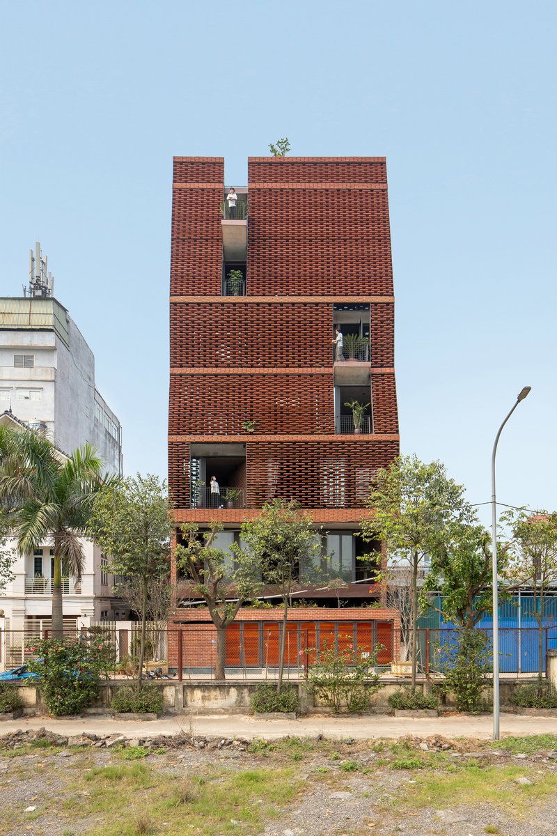 Street view of the patterned brick facade with recessed balconies and young trees in the foreground