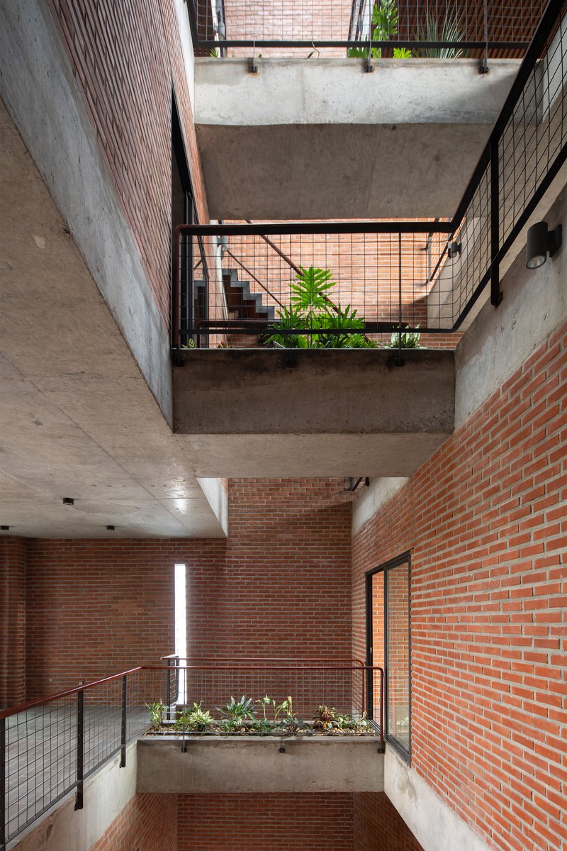 Interior atrium with stacked concrete balconies, red brick walls, and planted beds at each level